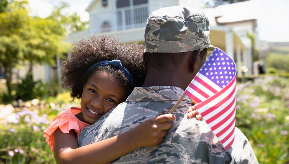 Girl hugging military father and holding mini American flag