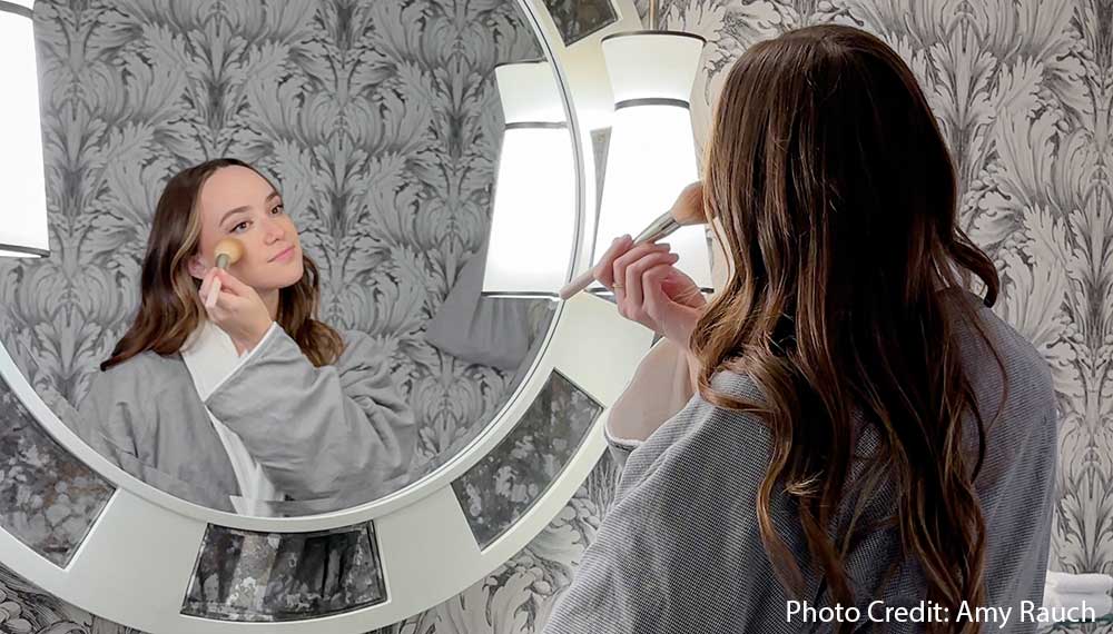 woman putting on make-up at mirror